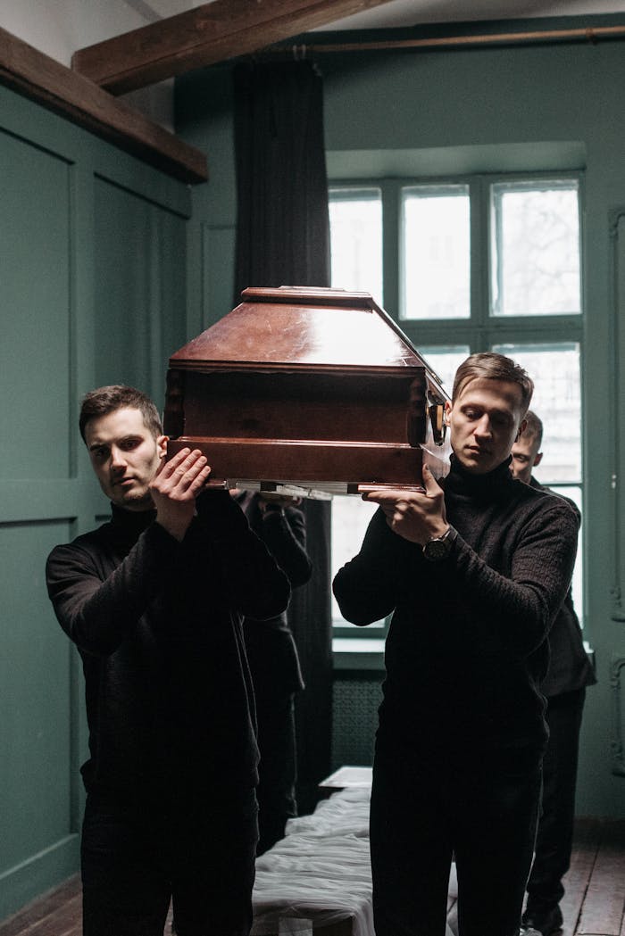 Mournful scene of pallbearers carrying a coffin inside a dimly lit room.